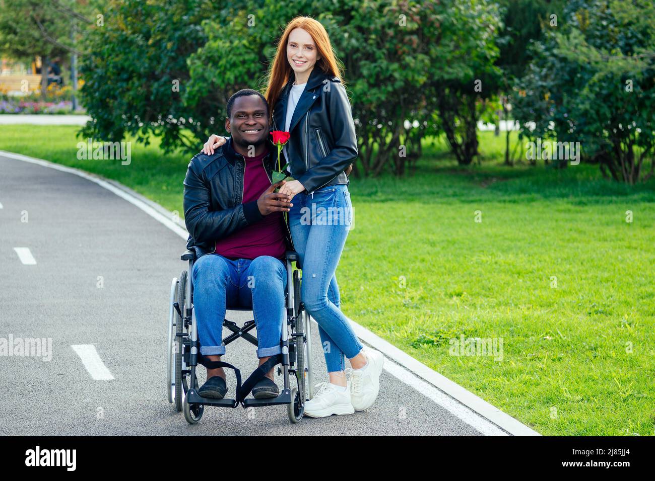 afro-amerikanischer Mann auf Rollstuhl sitzend, seine rothaarige Ingwer-Freundin Rolling Kinderwagen im Herbst Park. Mit romantischen Datum Stockfoto