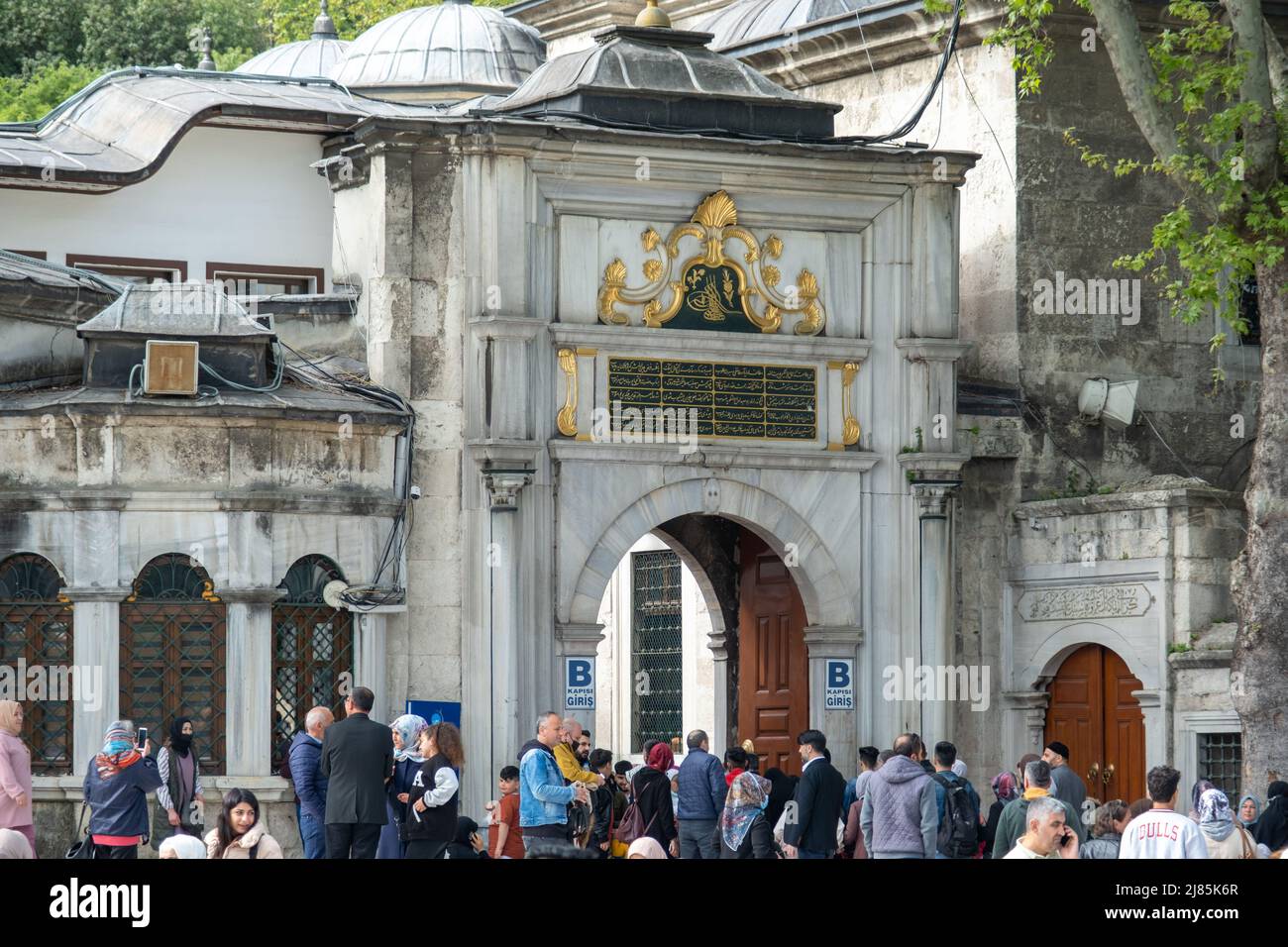 Viele Menschen mit einer Moschee-Tür im Hintergrund, islamische Kultur, heiliger Ort, Editorial Eyup Sultan Camii mit muslimischen Menschen, großes Holztor Stockfoto