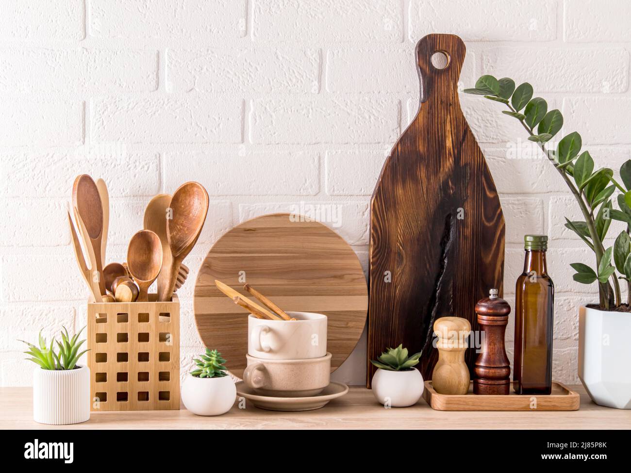 Verschiedene Arten von Küchenutensilien, Holzbretter, Gewürzbehälter, grüne Topfpflanze auf einer modernen Arbeitsplatte. Modische Küchenausstattung Stockfoto