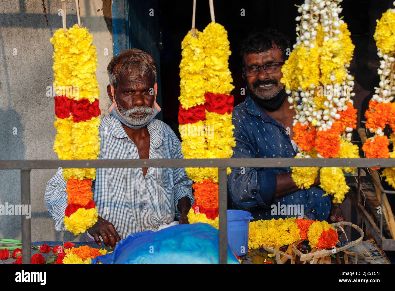 Zwei Blumenhändler, die durch hängende Blumengirlanden schauen, Tangassery, Thangassery, Kerala, Indien. Stockfoto