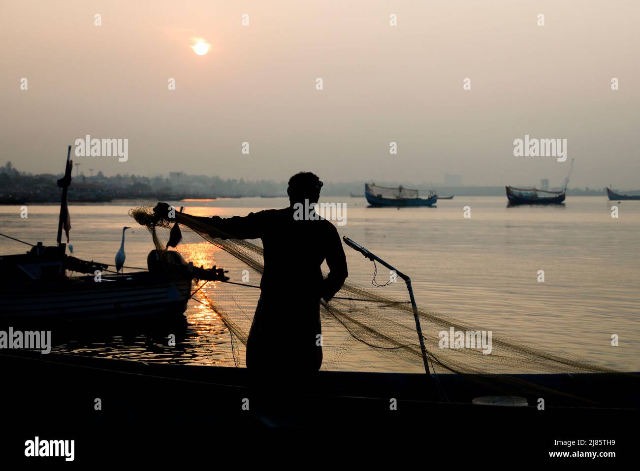 Silhouette eines Fischers, der in einem Boot mit Fischernetz steht, Tangassery, Kerala, Indien. Stockfoto