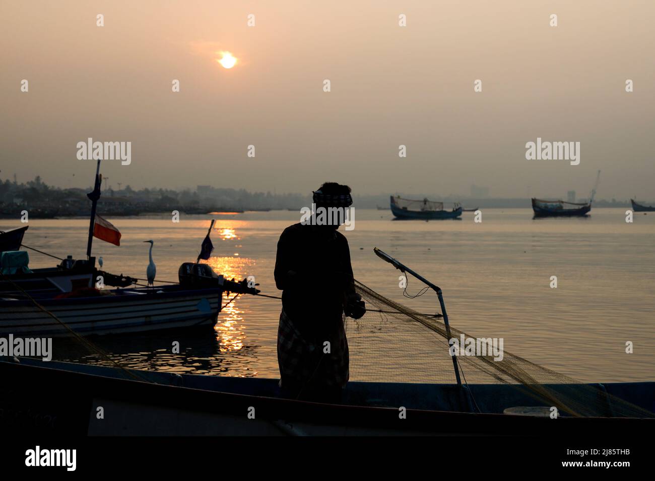 Silhouette eines Fischers, der in einem Boot mit Fischernetz steht, Tangassery, Kerala, Indien. Stockfoto