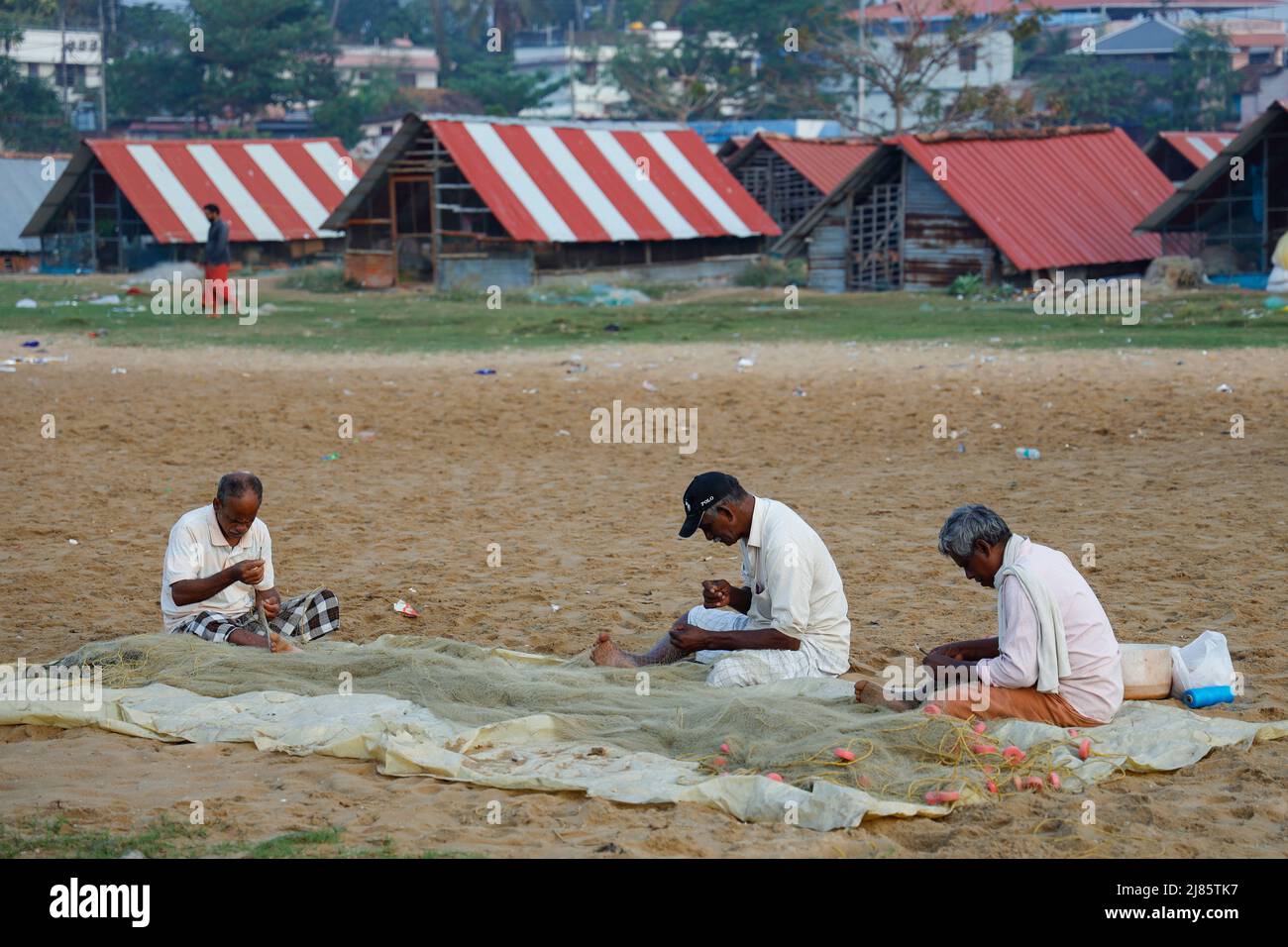 Drei Fischer, die am Strand sitzen und ihre Fischernetze ausbessern, Tangassery, Kerala, Indien. Stockfoto