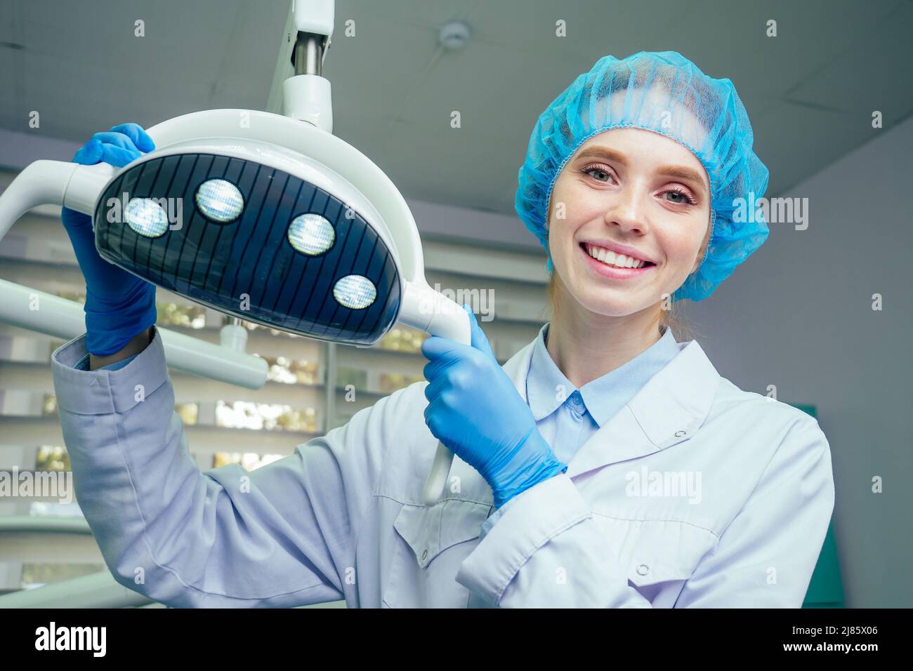 Porträt einer lächelnden Chirurgen in Operationsuniform im Operationssaal, die sich in der Nähe des Operationslichts im Labor aufstellt Stockfoto