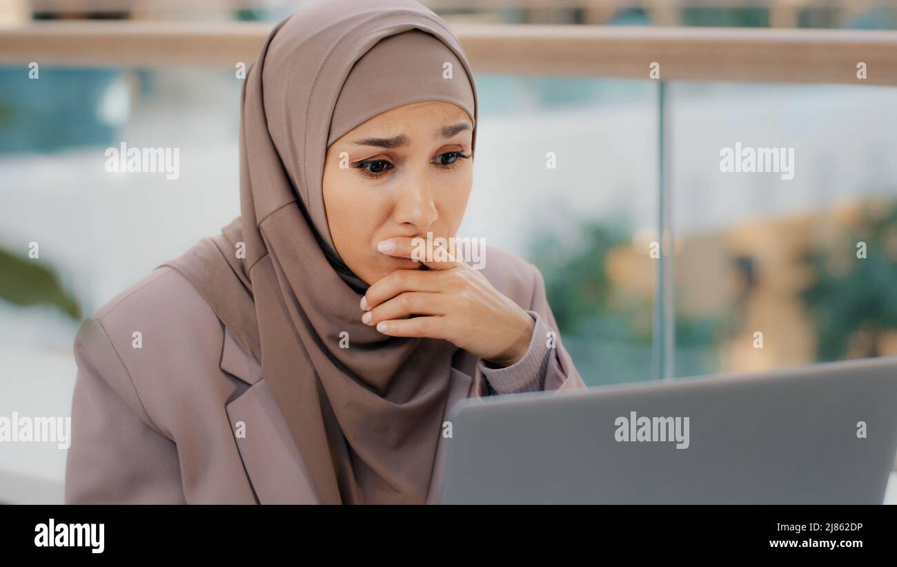 Traurige muslimische Studentin in Hijab, die E-Mails auf dem Laptop-Bildschirm liest, schockiert durch schlechte Nachrichten frustrierte Geschäftsfrau sorgt sich um finanzielle Probleme Stockfoto