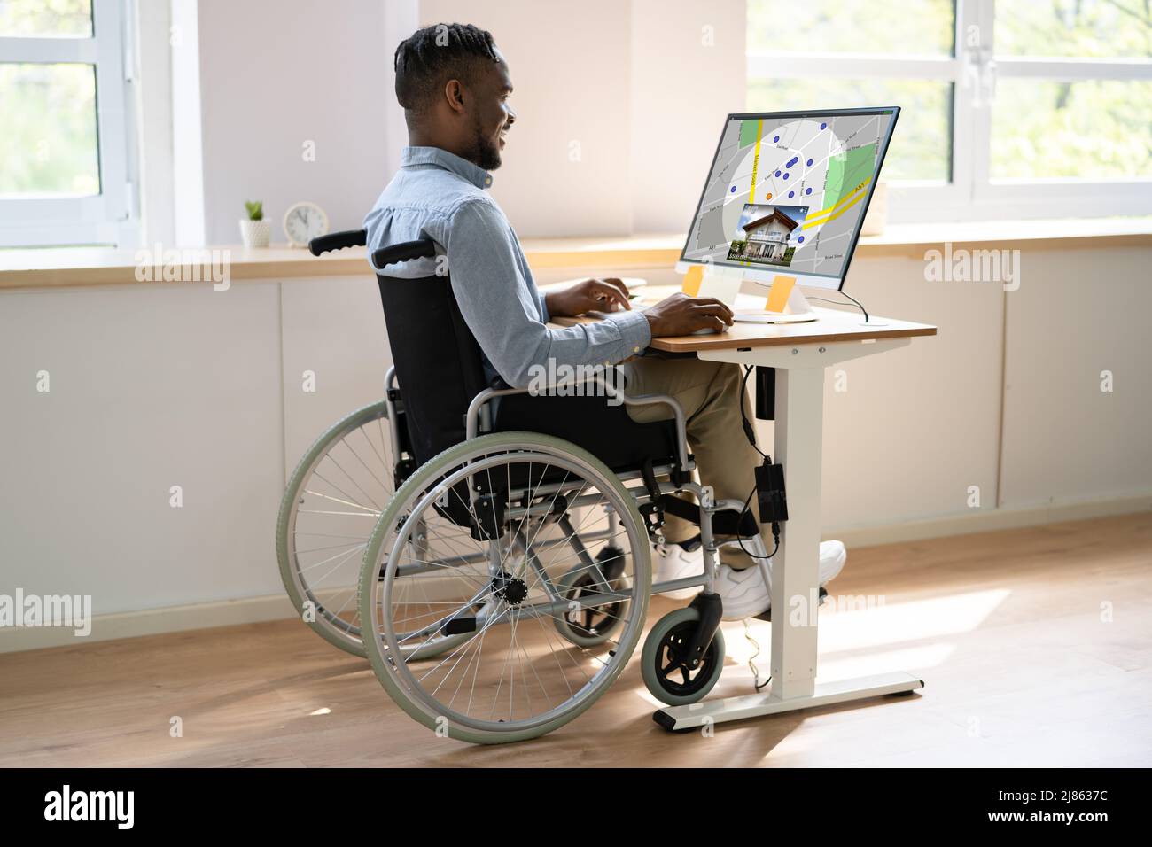 Arbeiter Im Rollstuhl Auf Der Suche Nach Immobilien Auf Computer Bei Der Arbeit Stockfoto