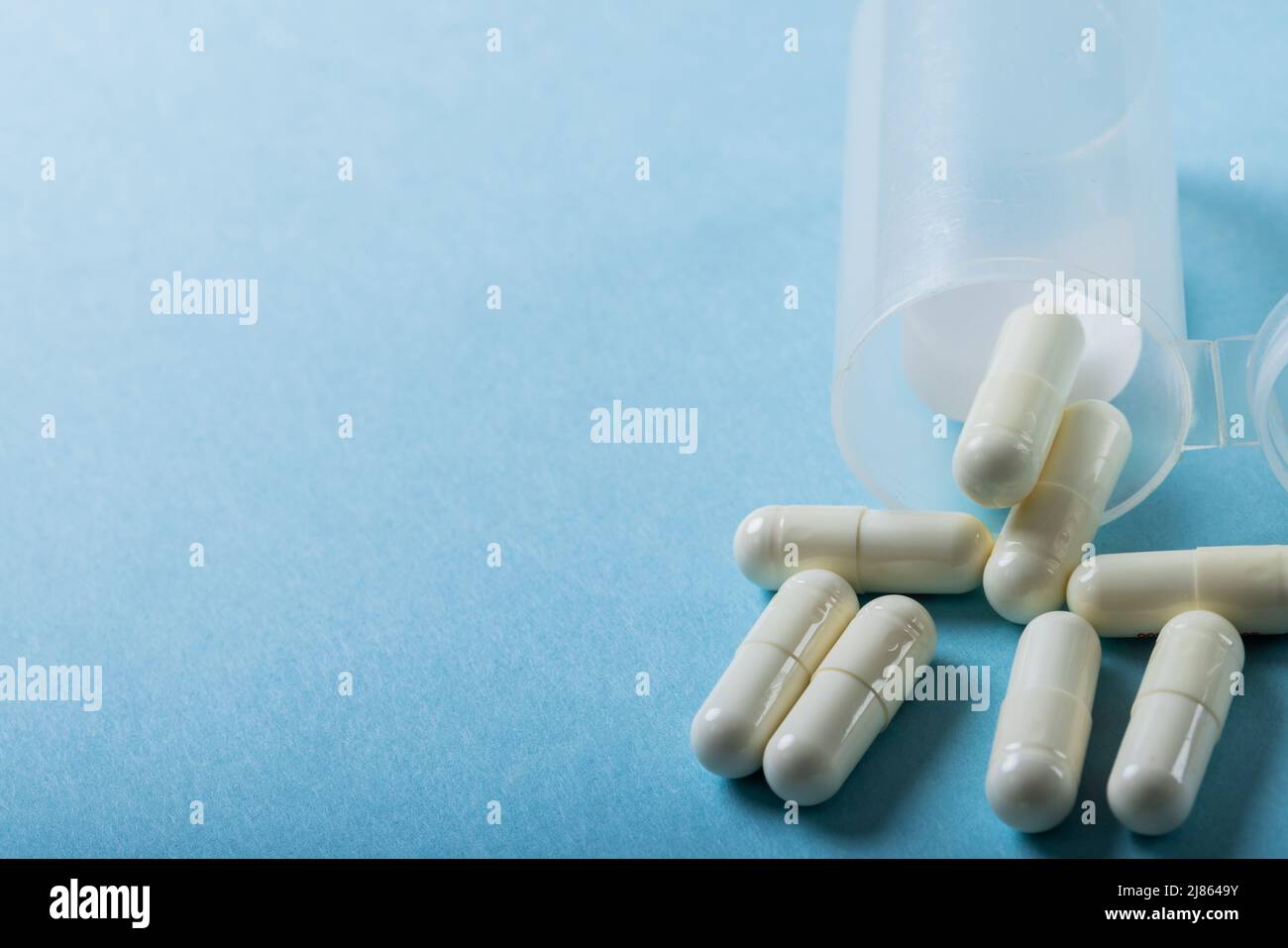 Nahaufnahme von weißen Kapseln, die aus der Flasche über blauem Hintergrund verschüttet wurden, mit großem Winkel, Kopierbereich Stockfoto