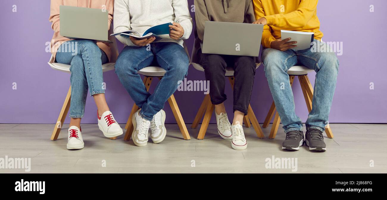 Junge Menschen mit Laptops und Notebooks sitzen in Reihe auf Stühlen auf dem Hintergrund einer violetten Wand. Stockfoto