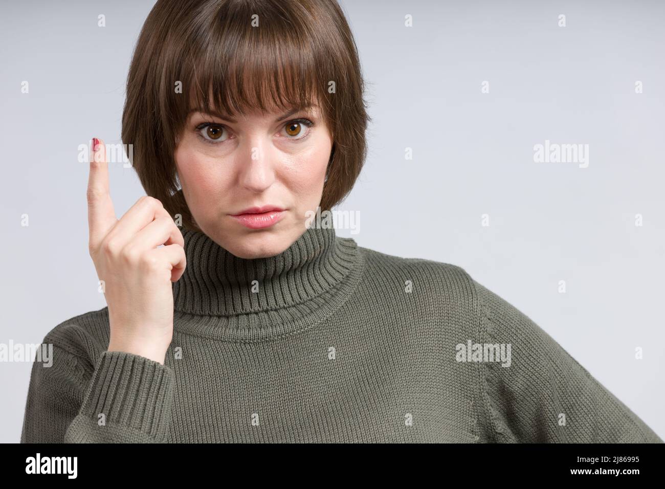 Junge lächelnde / glückliche Frau hat eine Idee und hebt ihren Zeigefinger Stockfoto