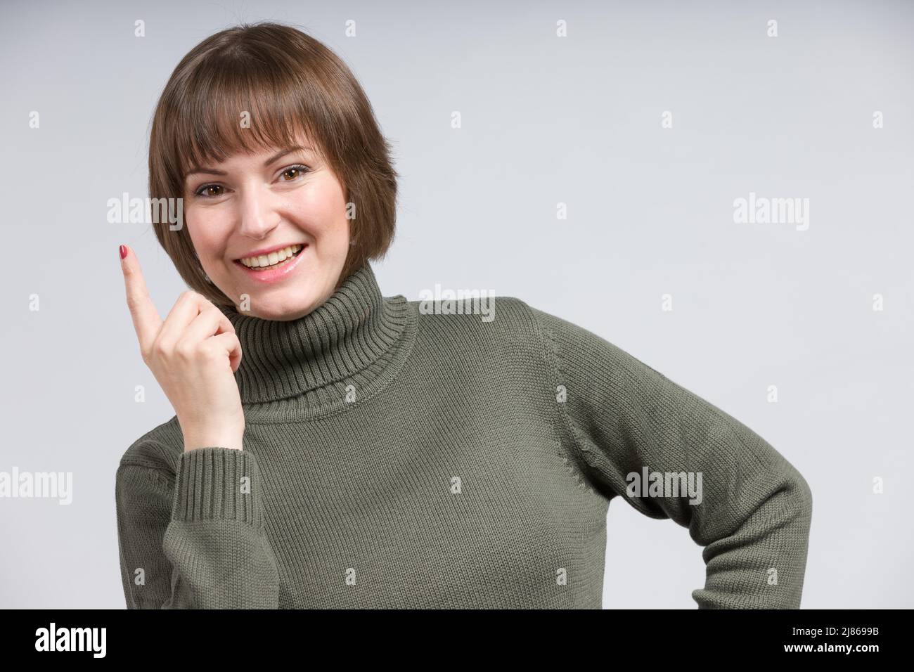 Junge lächelnde / glückliche Frau hat eine Idee und hebt ihren Zeigefinger Stockfoto