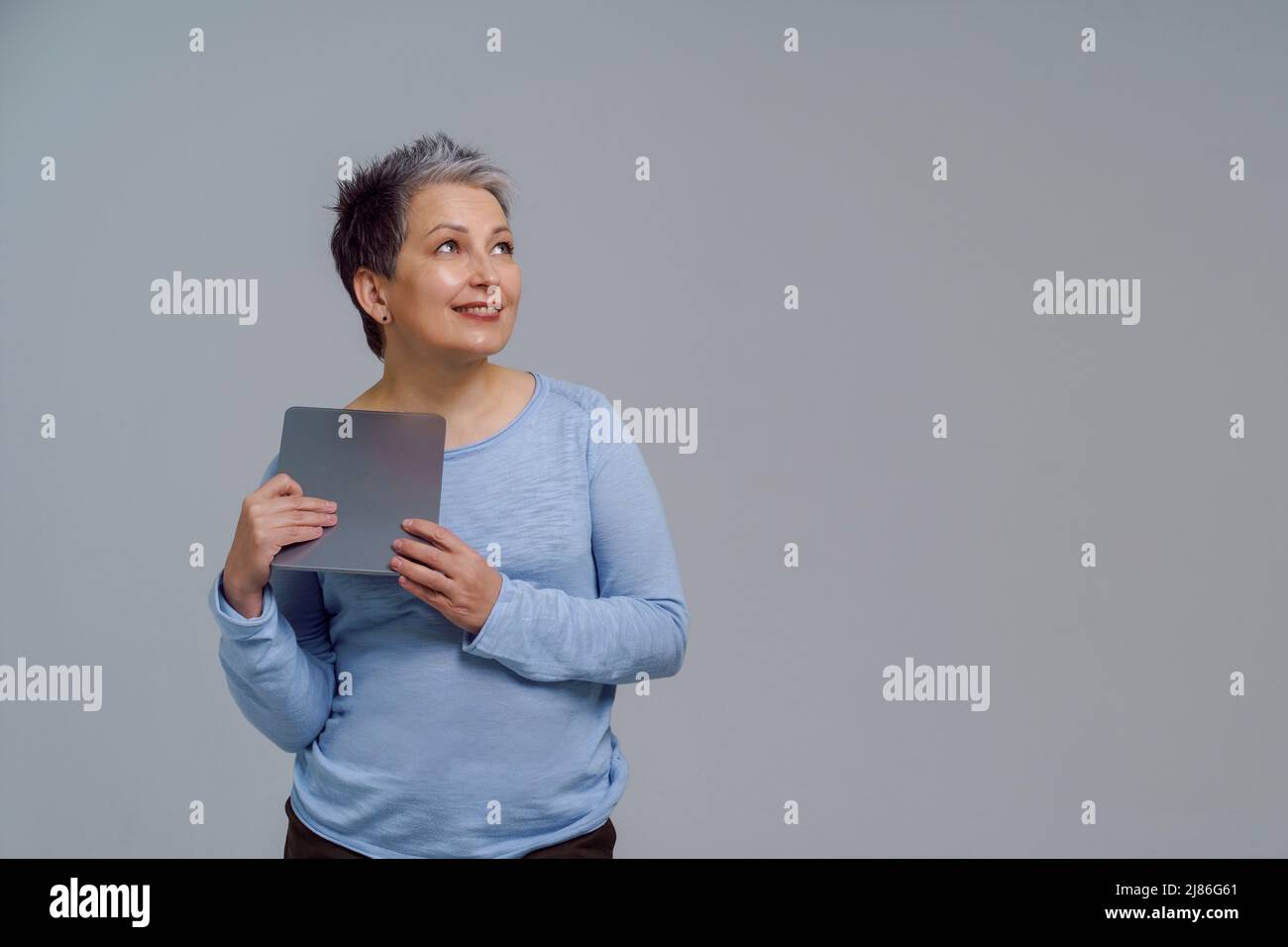 Träumen schöne reife grauhaarige Frau im Jahr 50s hält digitale Tablet arbeiten oder online einkaufen oder auf Social Media überprüfen. Hübsche Frau in blauer Bluse isoliert auf weißem Hintergrund. Getöntes Bild. Stockfoto