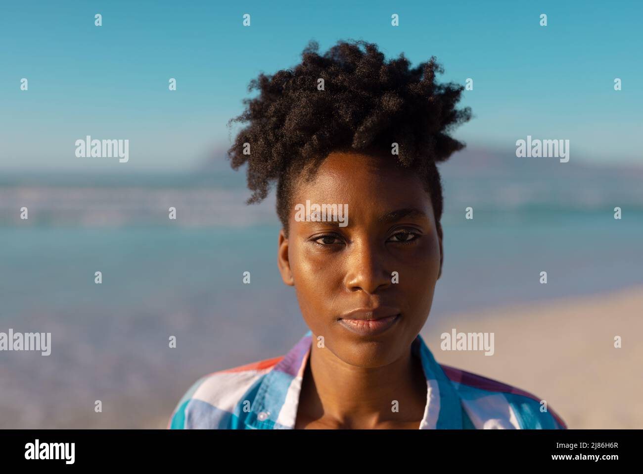 Nahaufnahme einer jungen afroamerikanischen Frau mit kurzen lockigen Haaren vor blauem Himmel am Strand Stockfoto