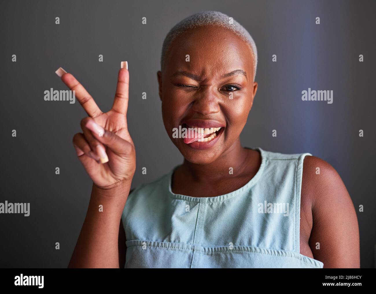 Ein junges schwarzes Modell mit rasierten Haaren posiert Friedenszeichen und Zunge aus Stockfoto