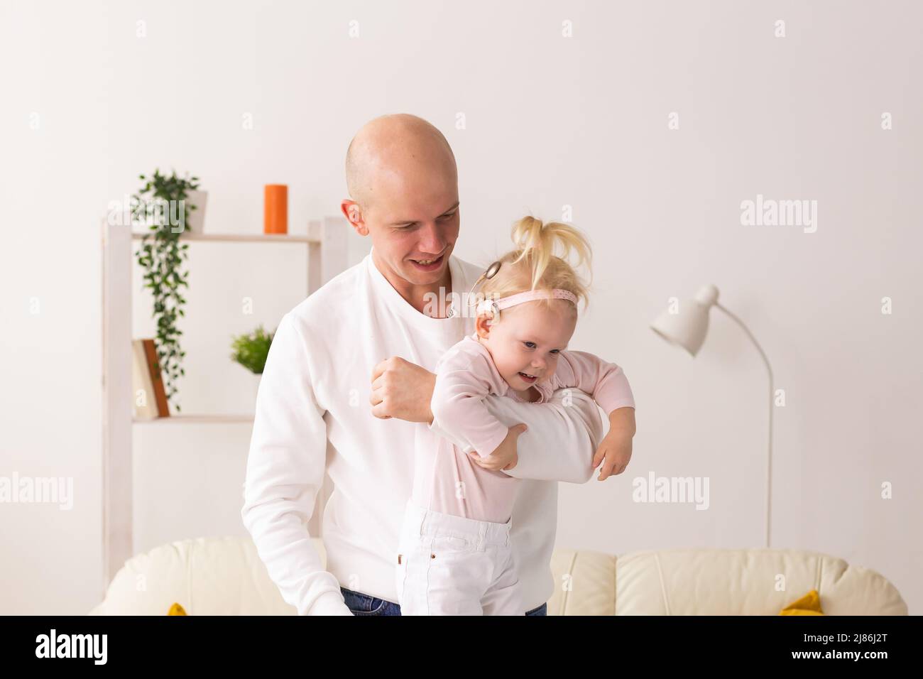 Baby mit Cochlea-Implantaten, das zu Hause mit ihrem Vater spielt. Taubheit und Medizintechnikkonzept Stockfoto