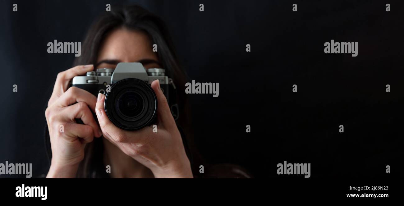 Junge Frau hält Fotokamera ist die Aufnahme Ihres Bildes isoliert auf schwarzem Hintergrund. Mädchen Fotograf Fokus auf Sie, Nahaufnahme Stockfoto