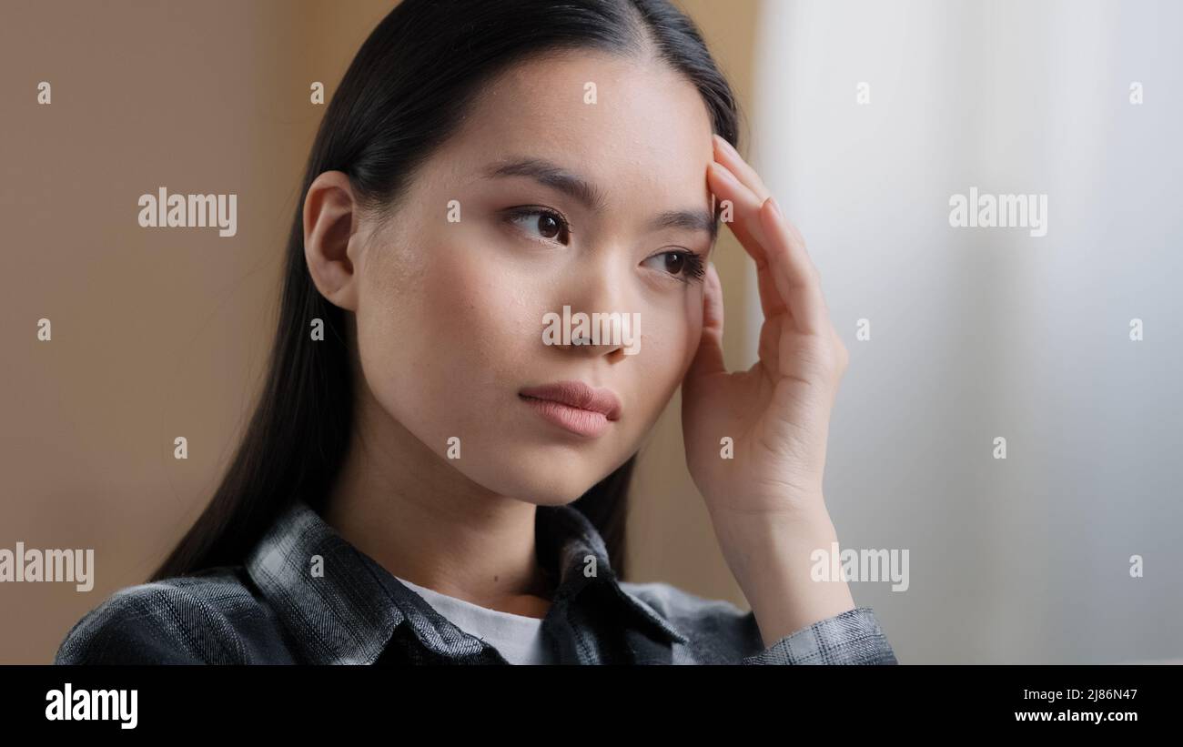 Portrait drinnen asiatische Mädchen tausendjährige Frau schwierige Gedanken Denken löst Problem reibt Stirn mit Hand fühlt Kopfschmerzen leidet an Migräne Stockfoto