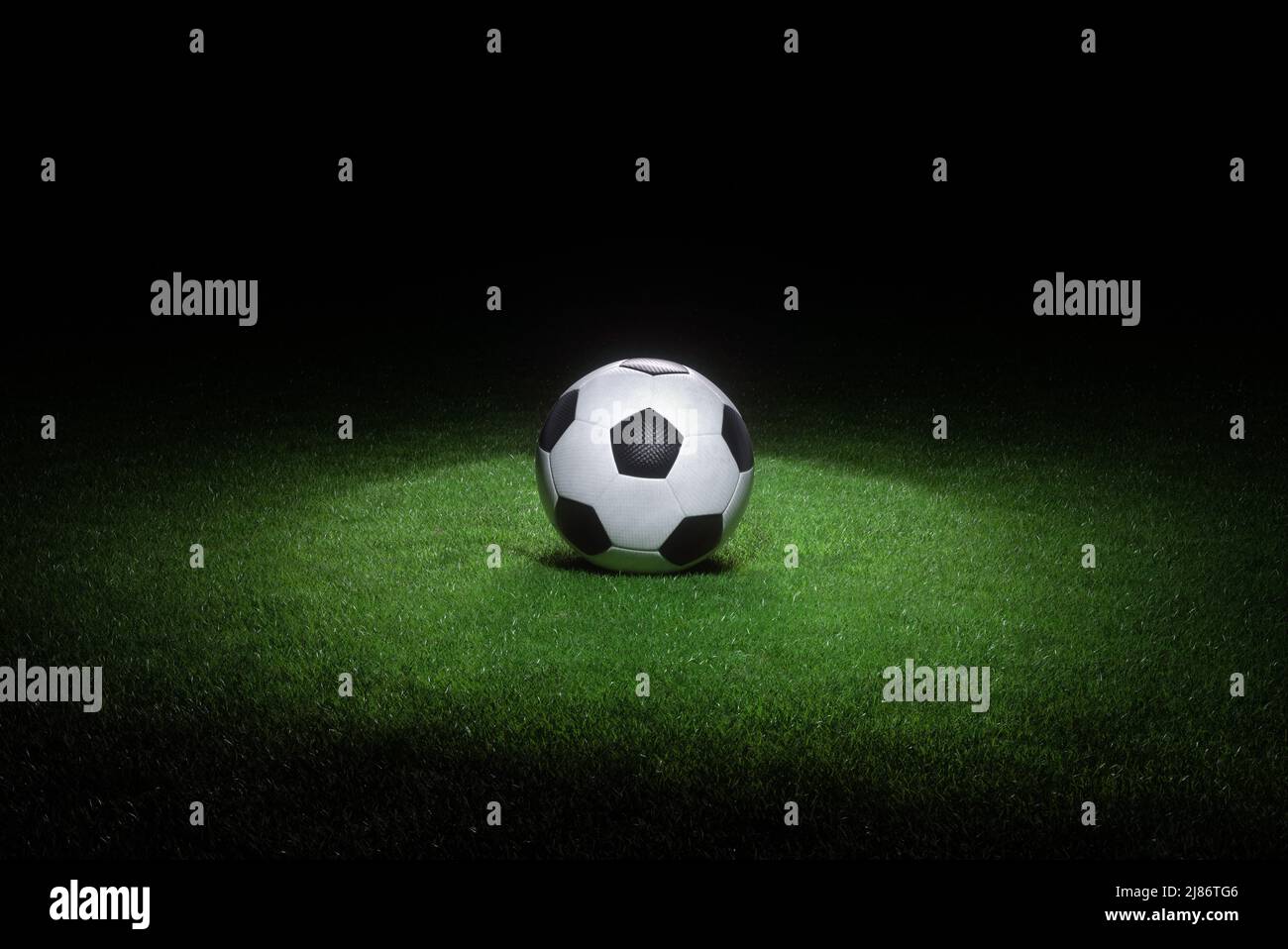 Schwarz-weißes Leder Fußball liegt auf frischem grünen Gras durch Scheinwerfer hervorgehoben. Abstraktes Thema der Sportausrüstung. Stockfoto