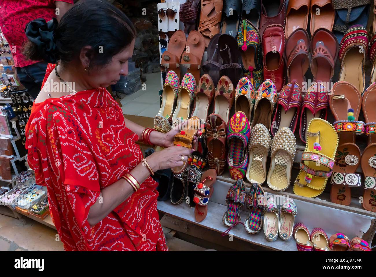 Jaisalmer, Rajasthan, Indien - 13. Oktober 2019 : Indische Frau, die Paare von Rajasthani Damenschuhen auf dem Display zum Verkauf überprüft. Jaisalmer, Rajasthan, In Stockfoto