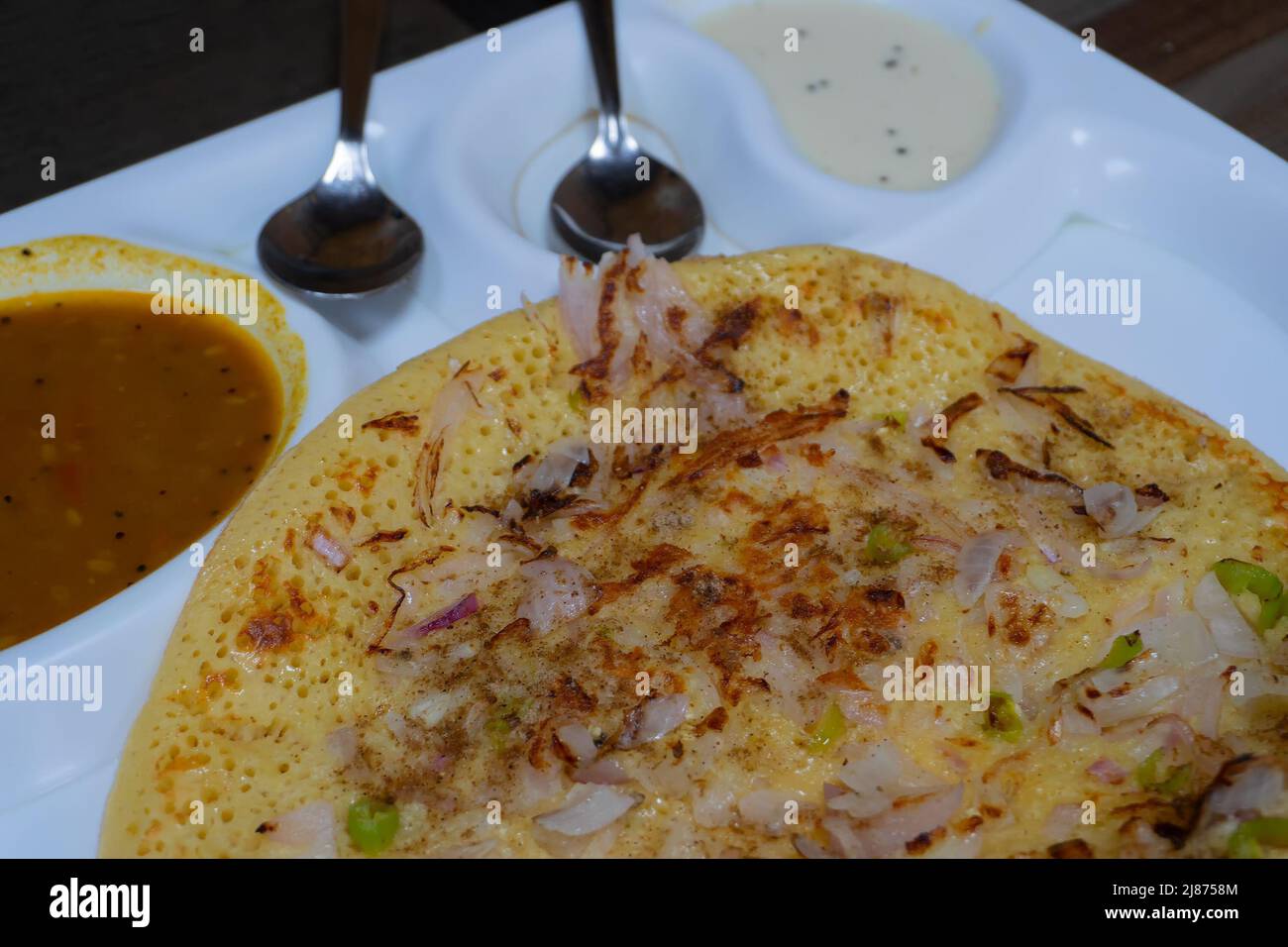 Uttapam wird mit Chutney auf einem weißen Teller serviert, einem indischen Gemüsegericht. Stockfoto