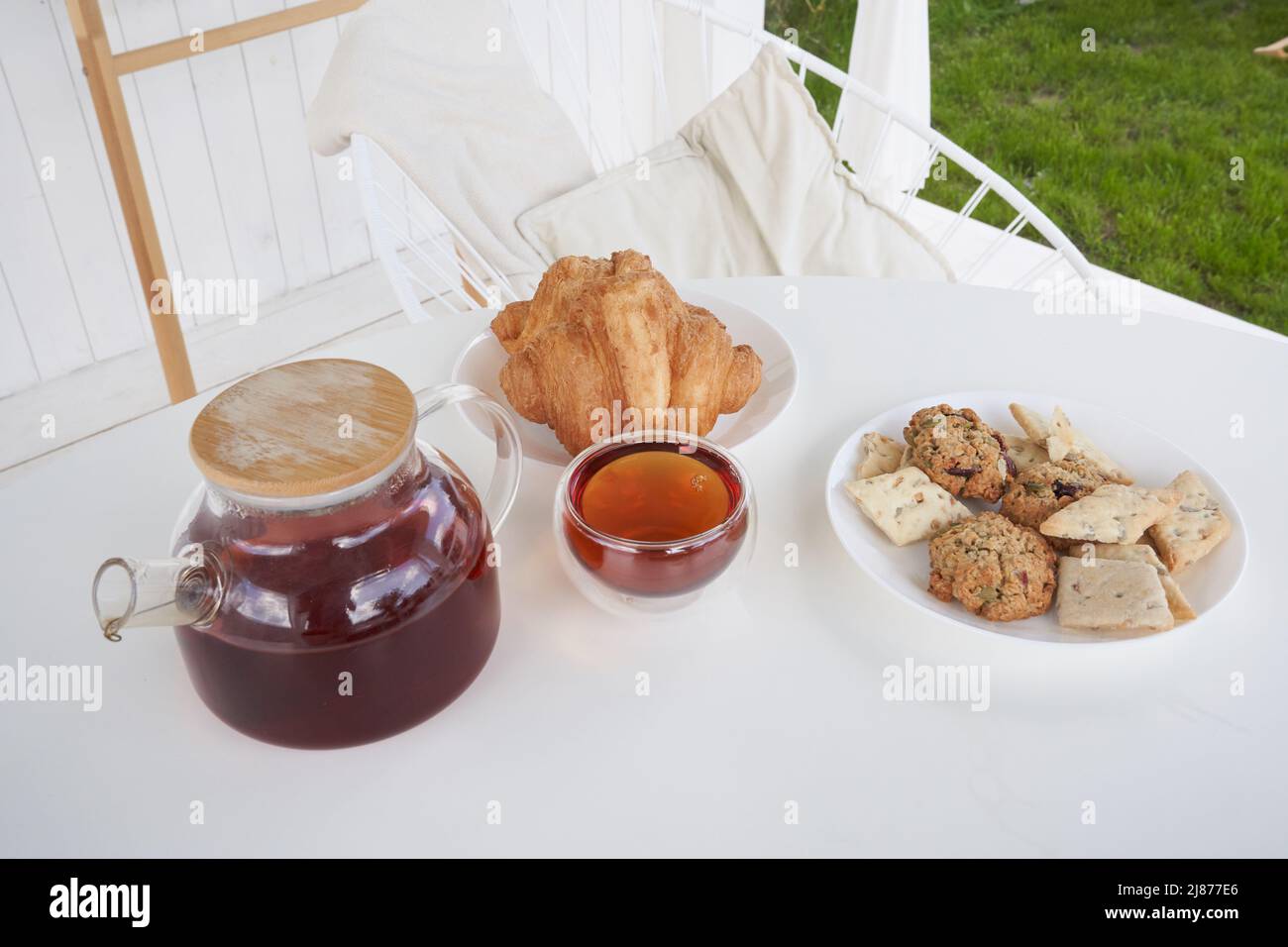 Sonntagsfrühstück im Hinterhof der Hütte. Frische süße Croissants mit Keksen auf dem Tisch. Transparente Teekane aus Glas mit gebrühtem Tee. Hochwertige Fotos Stockfoto