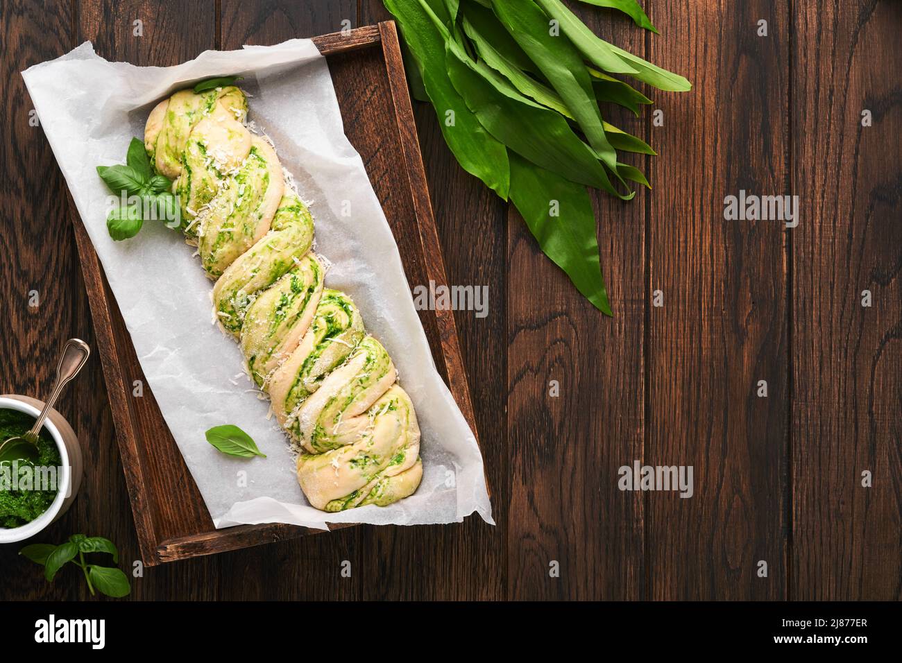 Geflochtenes Bärlauch-Pesto Brioche. Hausgemachtes rohes oder rohes frisches Pull-Apart-Brot mit Bärlauch-Pesto auf Holzbrett auf Holzhintergrundtisch. Stockfoto