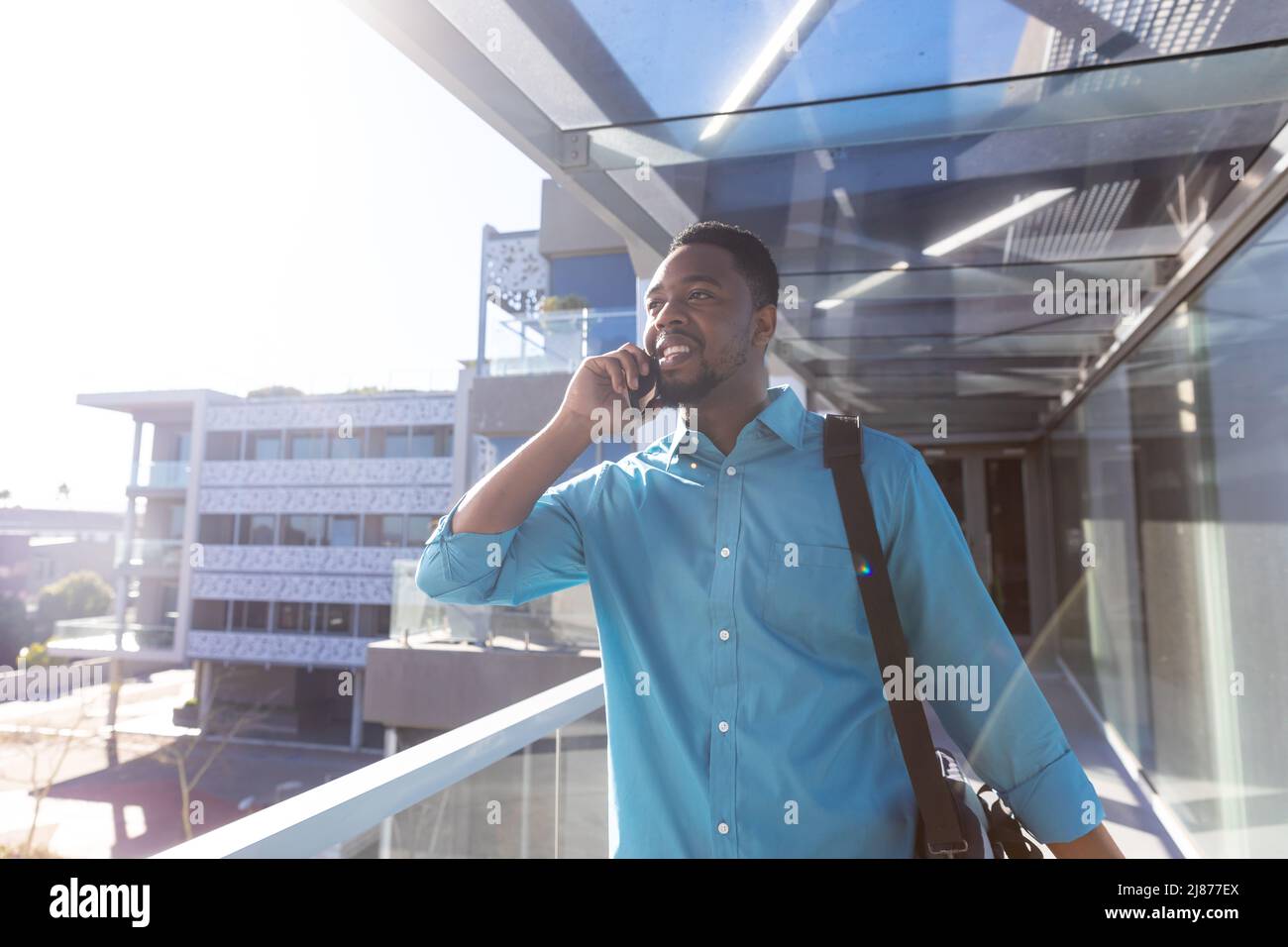 Lächelnder afroamerikanischer Geschäftsreisender, der auf dem Smartphone spricht und auf dem Flughafenflur läuft Stockfoto