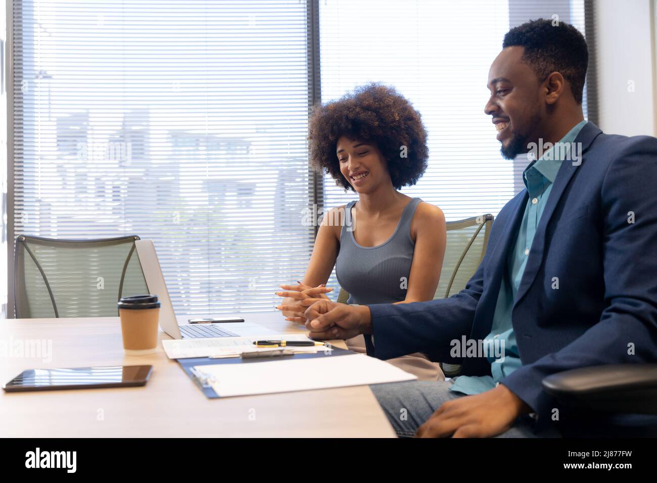 Lächelnder, multirassischer Geschäftsmann und Geschäftsfrau diskutieren während der Sitzung im Sitzungssaal Stockfoto