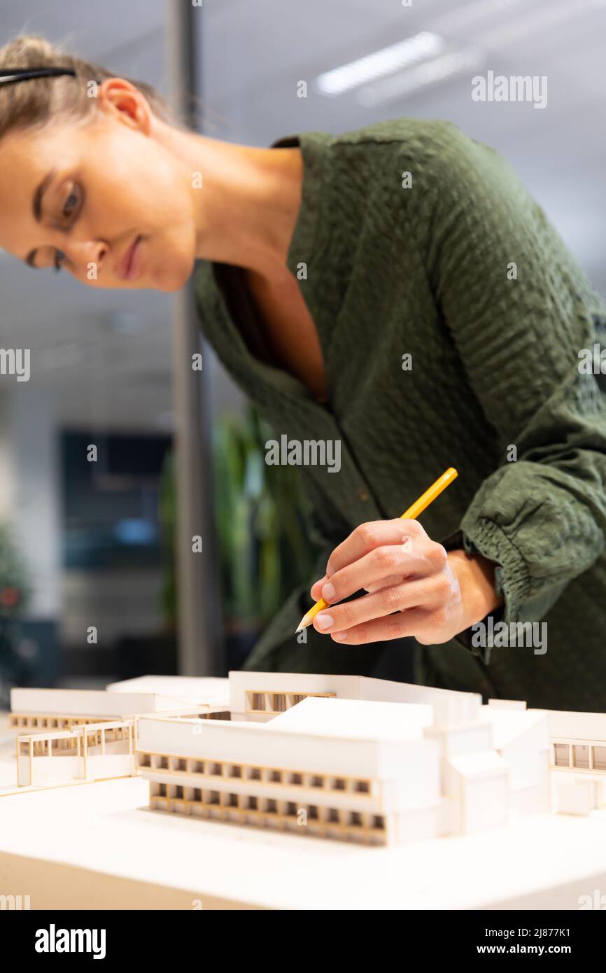 Kaukasische Architektin analysiert Architekturmodell auf Schreibtisch mit Bleistift am modernen Arbeitsplatz Stockfoto