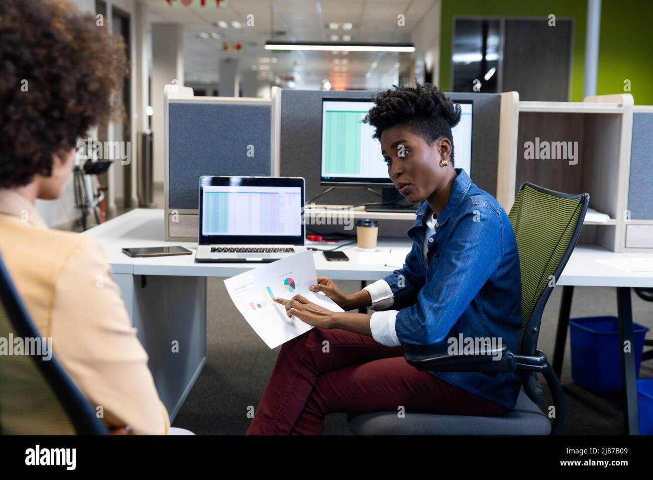 Selbstbewusste afroamerikanische Geschäftsfrau erklärt der hispanischen Kollegin in Kabine das Dokument Stockfoto