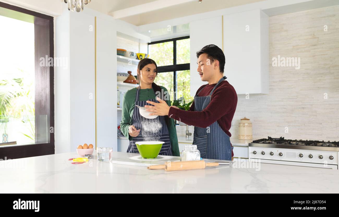 Asiatische junge Frau schaut auf männlichen Partner sieben Mehl in der Küche zu Hause Stockfoto