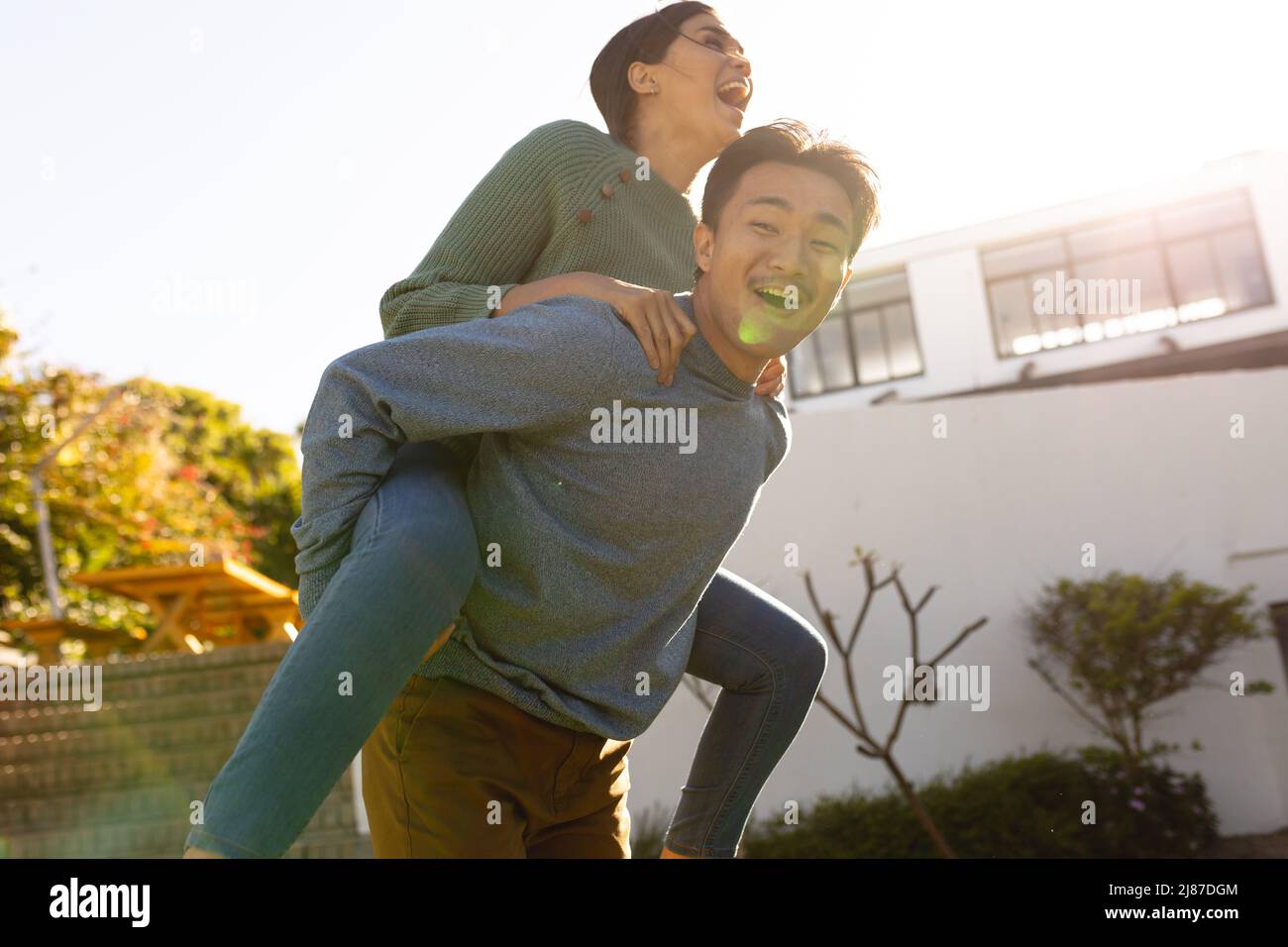 Verspielt junge asiatische Mann Huckepack Freundin im Hof während sonnigen Tag, kopieren Raum Stockfoto