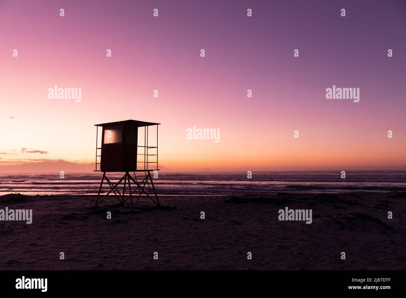 Blick auf die Silhouette Rettungsschwimmerhütte am Sandstrand mit Blick auf das Meer und den klaren, violetten Himmel Stockfoto