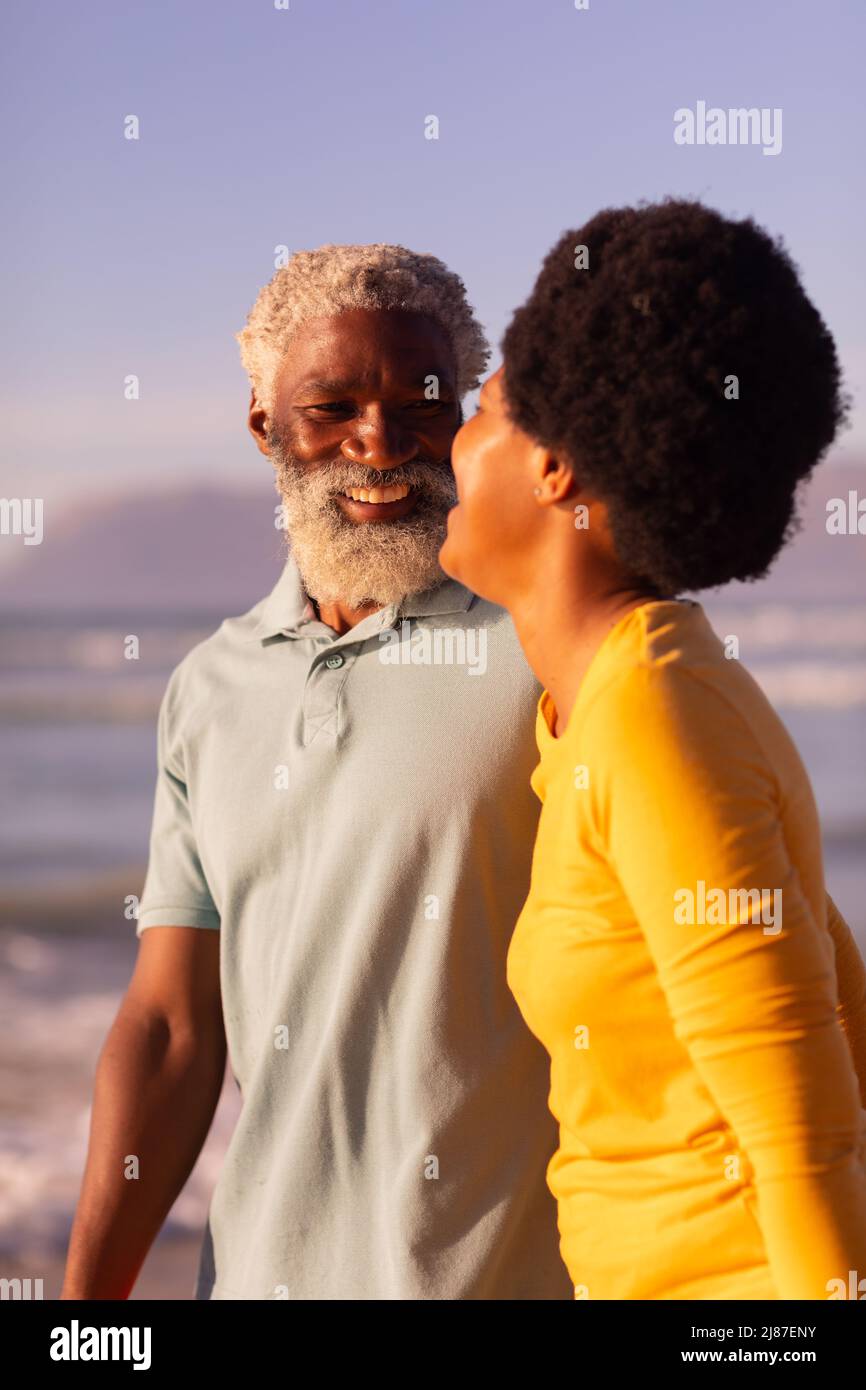 Fröhliches afroamerikanisches Paar, das am Strand steht und beim Sonnenuntergang einen klaren blauen Himmel hat Stockfoto