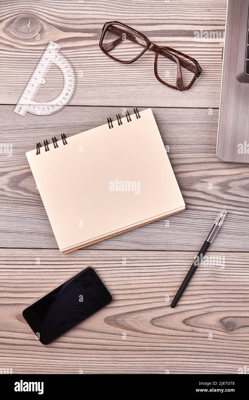 Vertikale Aufnahme, Draufsicht, leerer Notizblock für den Kopierbereich. Brillen mit Lineal und Smartphone auf dem Schreibtisch. Unordentliches Schreibtisch-Konzept. Stockfoto
