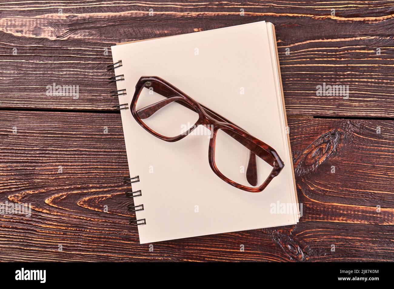 Draufsicht flacher Notizblock mit Brille. Brauner Holzschreibtisch im Hintergrund. Stockfoto