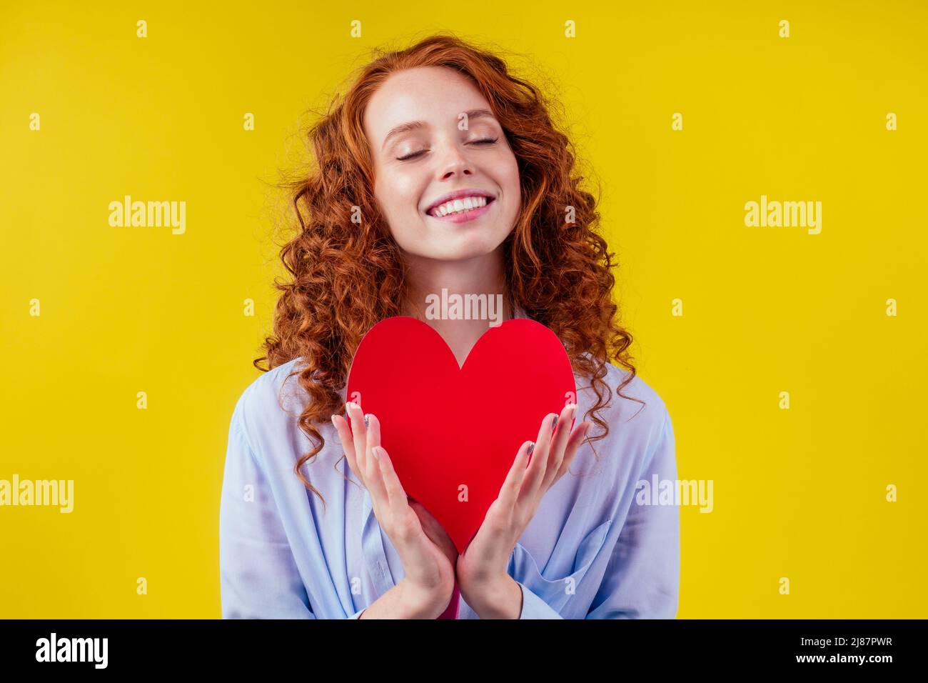 Schwanger Rotschopf Ingwer lockig Frau hält Papier Herz in Studio gelbe Wände.Valentinstag Stockfoto