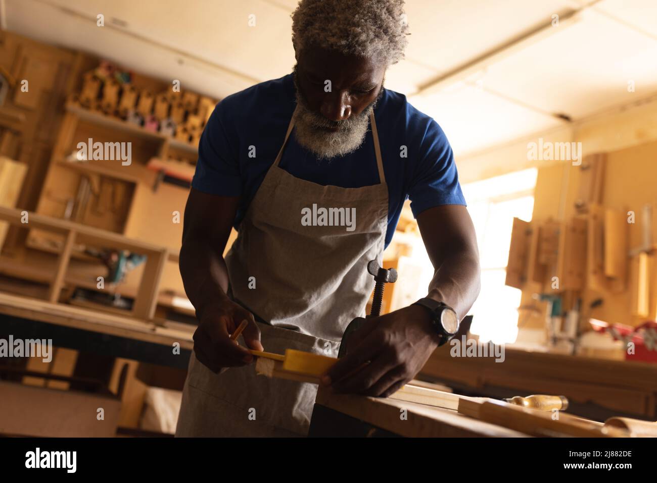 afroamerikanischer reifer Zimmermann in Schürze, der in der Werkstatt arbeitet Stockfoto