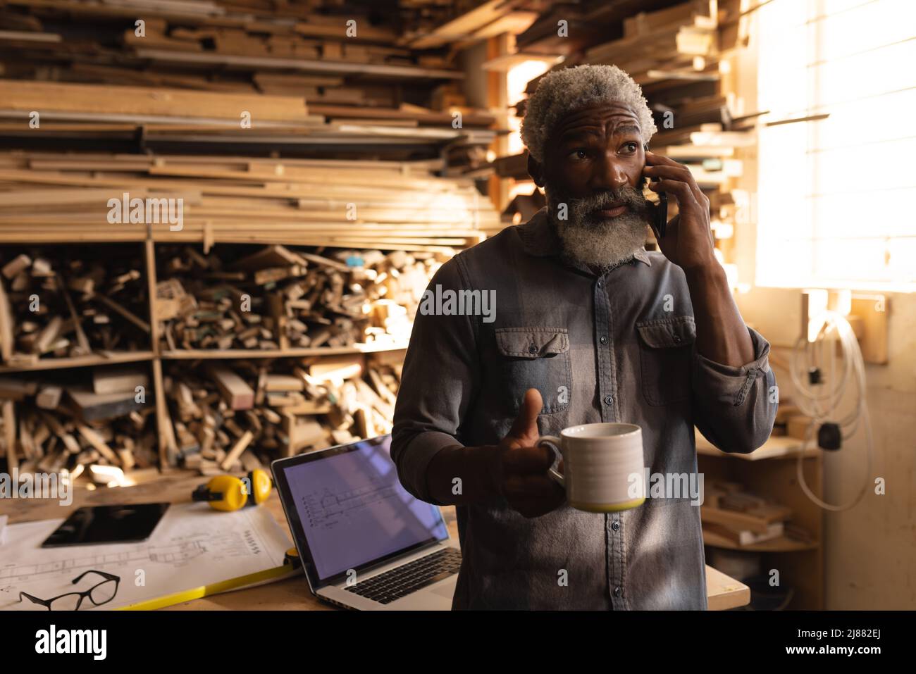 Kontemplativer afroamerikanischer reifer Zimmermann, der in der Holzwerkstatt Kaffee getrunken hat Stockfoto