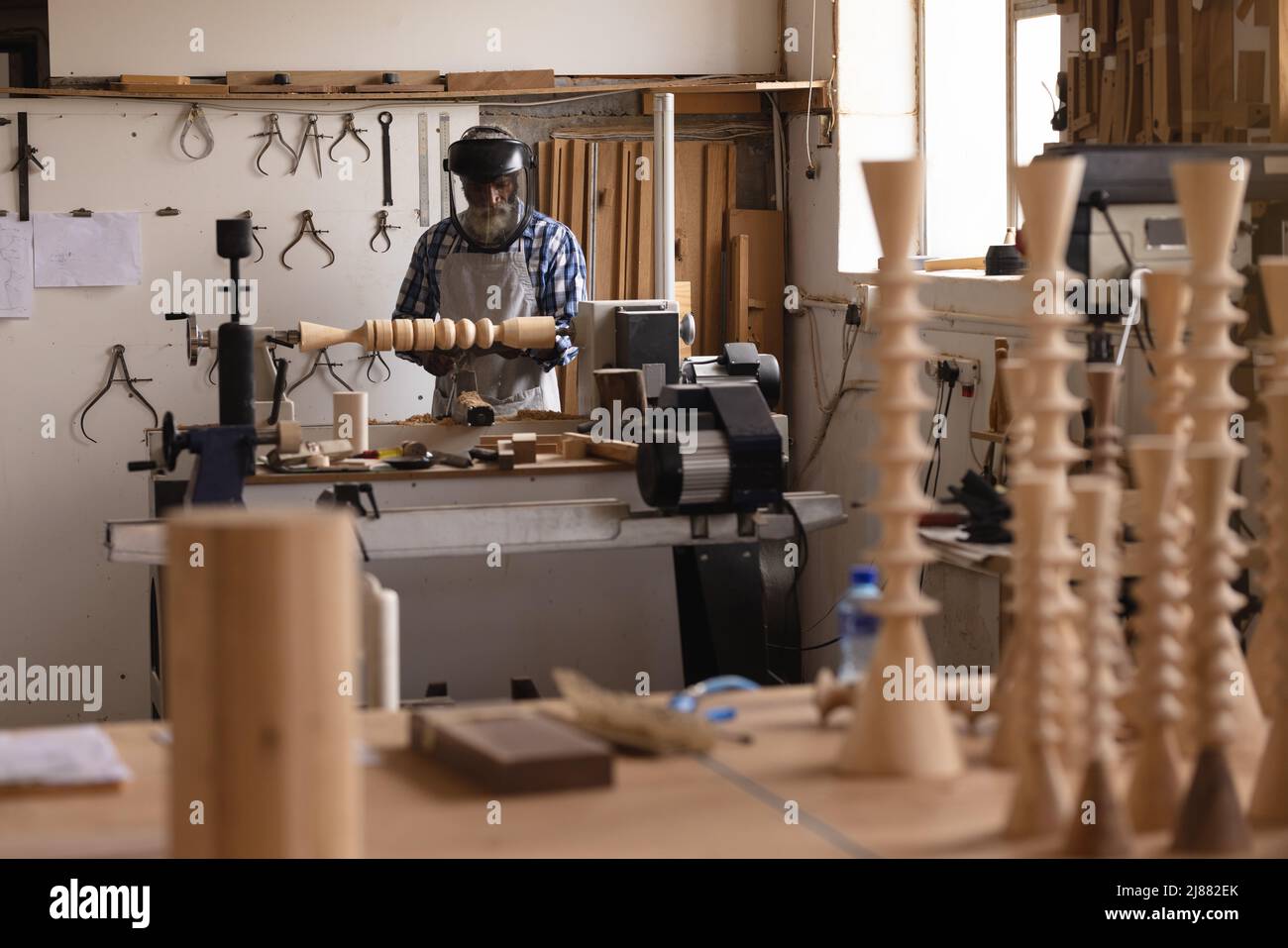 afroamerikanischer reifer Tischler in Sicherheitsgesicht, der Holz in der Werkstatt formt und schnitzt Stockfoto