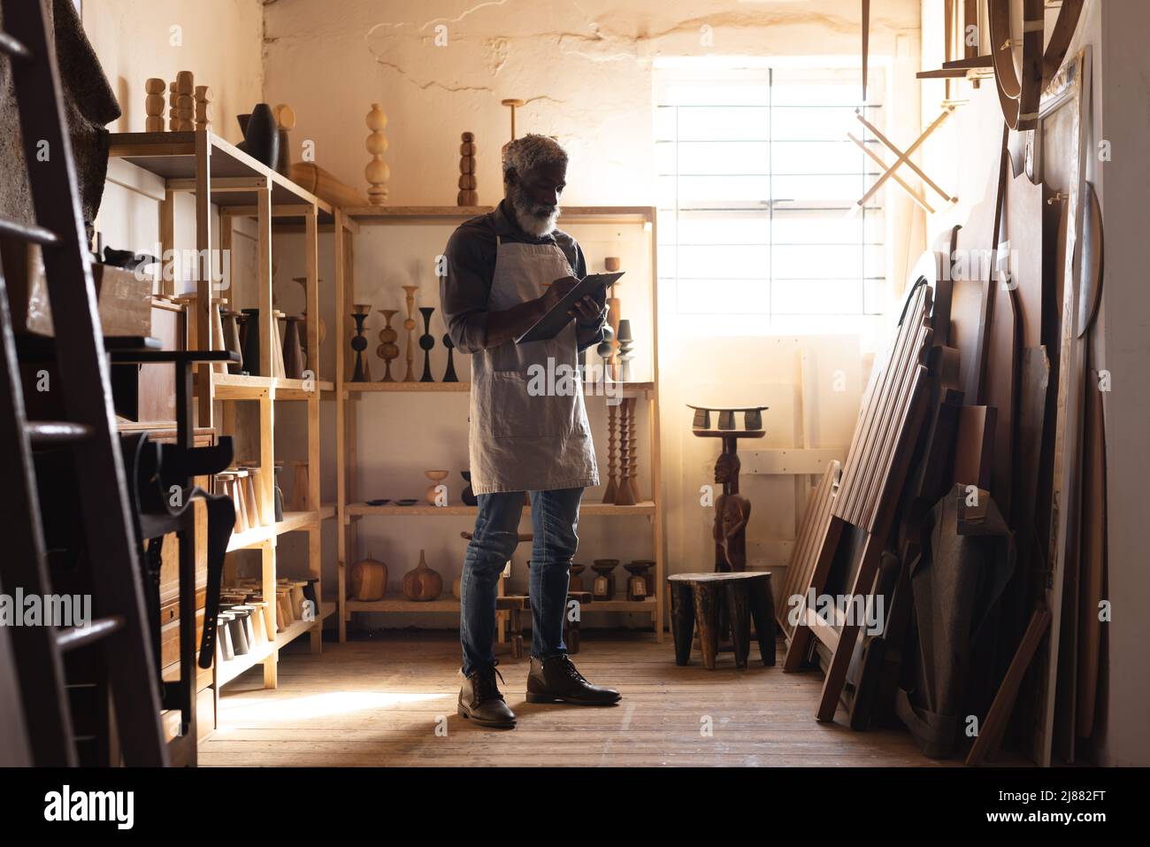 Die ganze Länge des afroamerikanischen reifen Zimmermanns, der in Notizblock schreibt, während er in der Werkstatt arbeitet Stockfoto