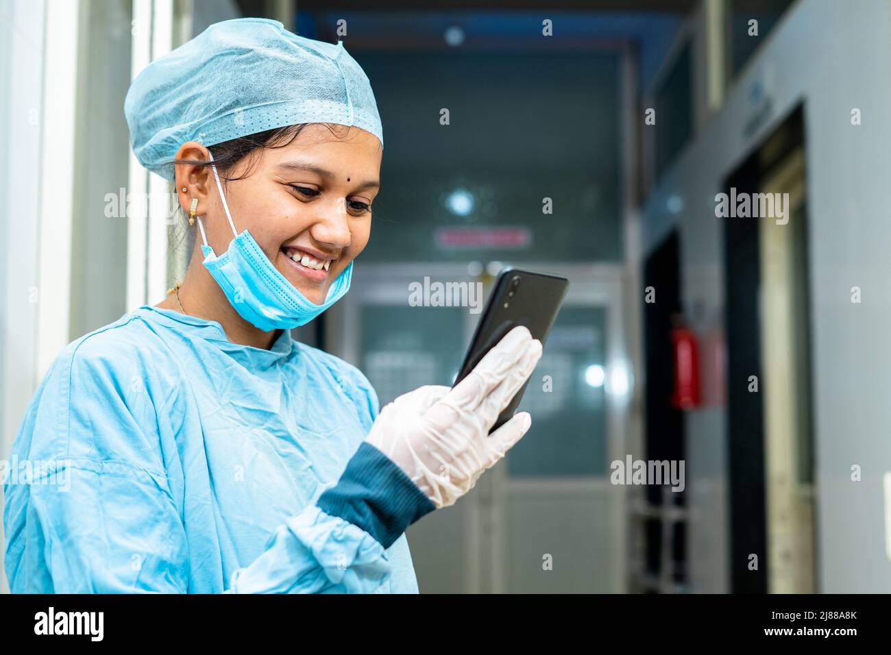Glücklich lächelnder Arzt beschäftigt mit Handy im Krankenhaus Korridor - Konzept der Verwendung von Social Medica, Technologie und Internet Stockfoto