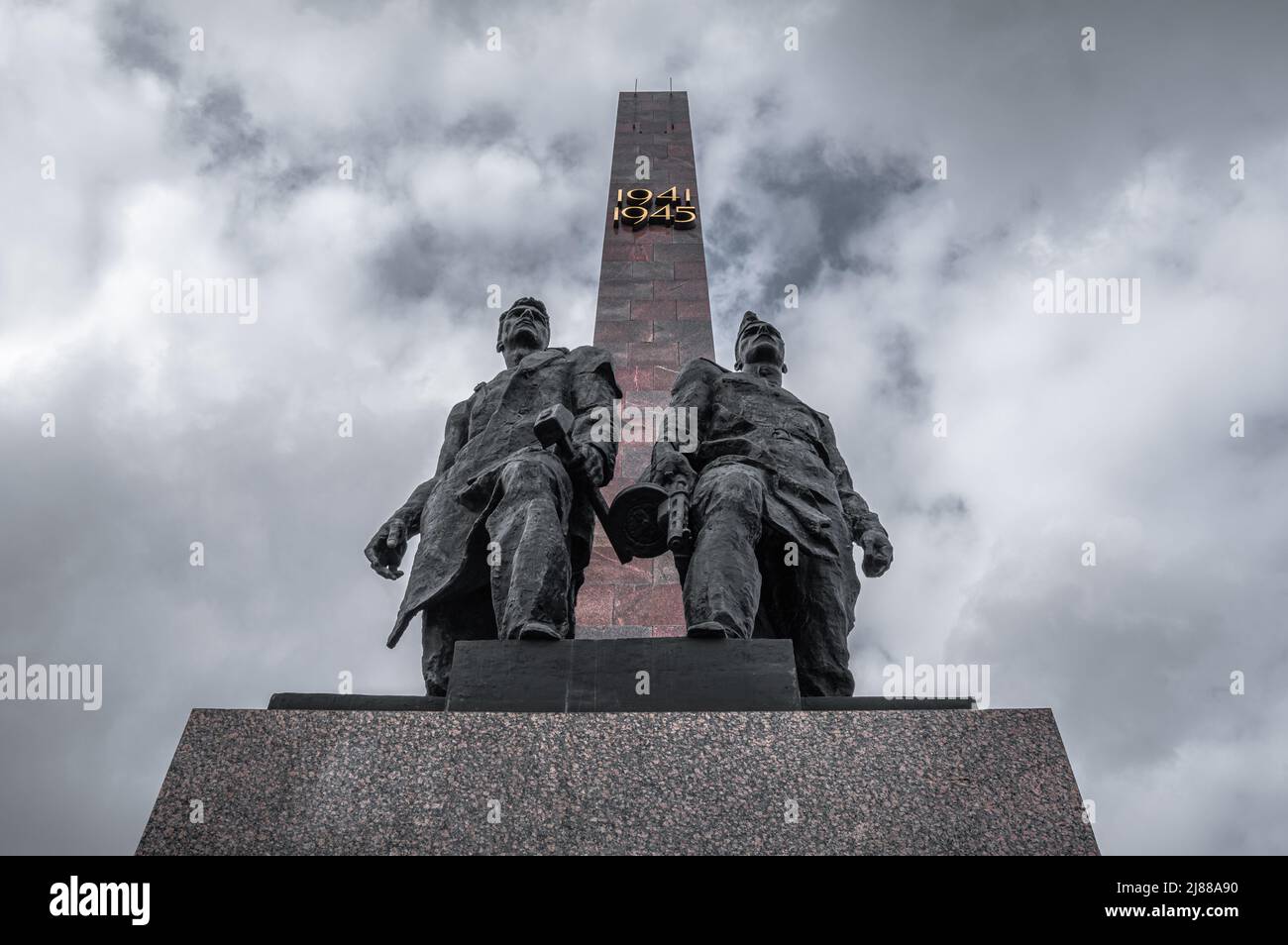 Denkmal für sowjetische Soldaten gegen den riesigen Obelisken und den wolkigen Himmel. Fragment des Gedenkkomplexes. Sankt Petersburg, Russland. Stockfoto
