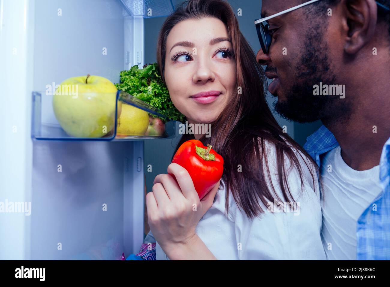 Blick auf den Kühlschrank:afroamerikaner Mann mit asiatischer Frau nehmen ein Gemüse mit offener Tür Stockfoto