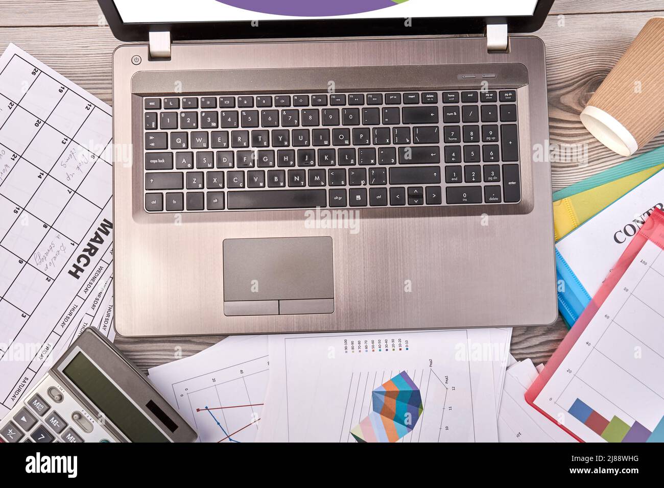 Silberner Laptop von oben auf dem Schreibtisch. Taschenrechner und Papiere mit Tabellen. Stockfoto