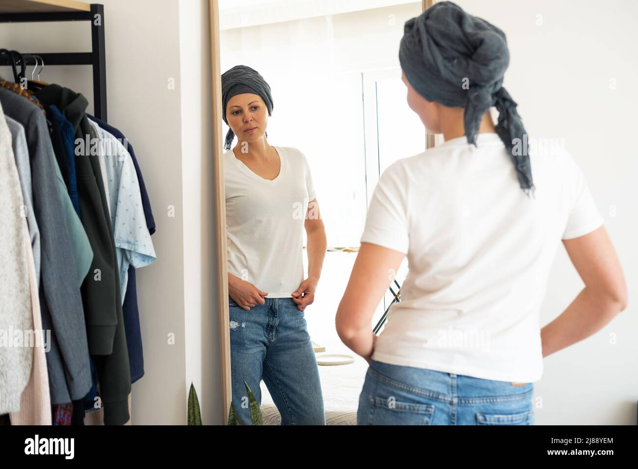 Eine Frau in einem weißen T-Shirt probiert vor einem Spiegel Kleidung an. Stockfoto