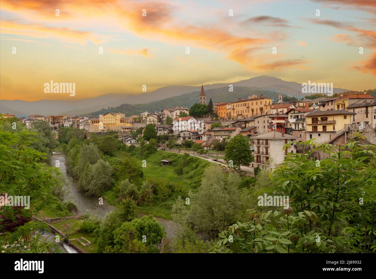 Dronero, Piemont, Italien: Blick auf das alte Dorf im Maira-Tal mit dem Fluss Maira. Landschaft mit bunt bewölktem Sonnenuntergang Himmel Stockfoto