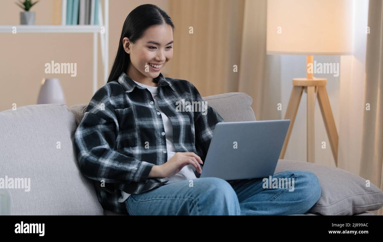 Asian 20s Mädchen Benutzer Millennial weiblich Student freiberuflich Frau chatten Internet mit Laptop Hause Sofa spielen Computer-Spiel lächelnd glücklich Wahl Stockfoto