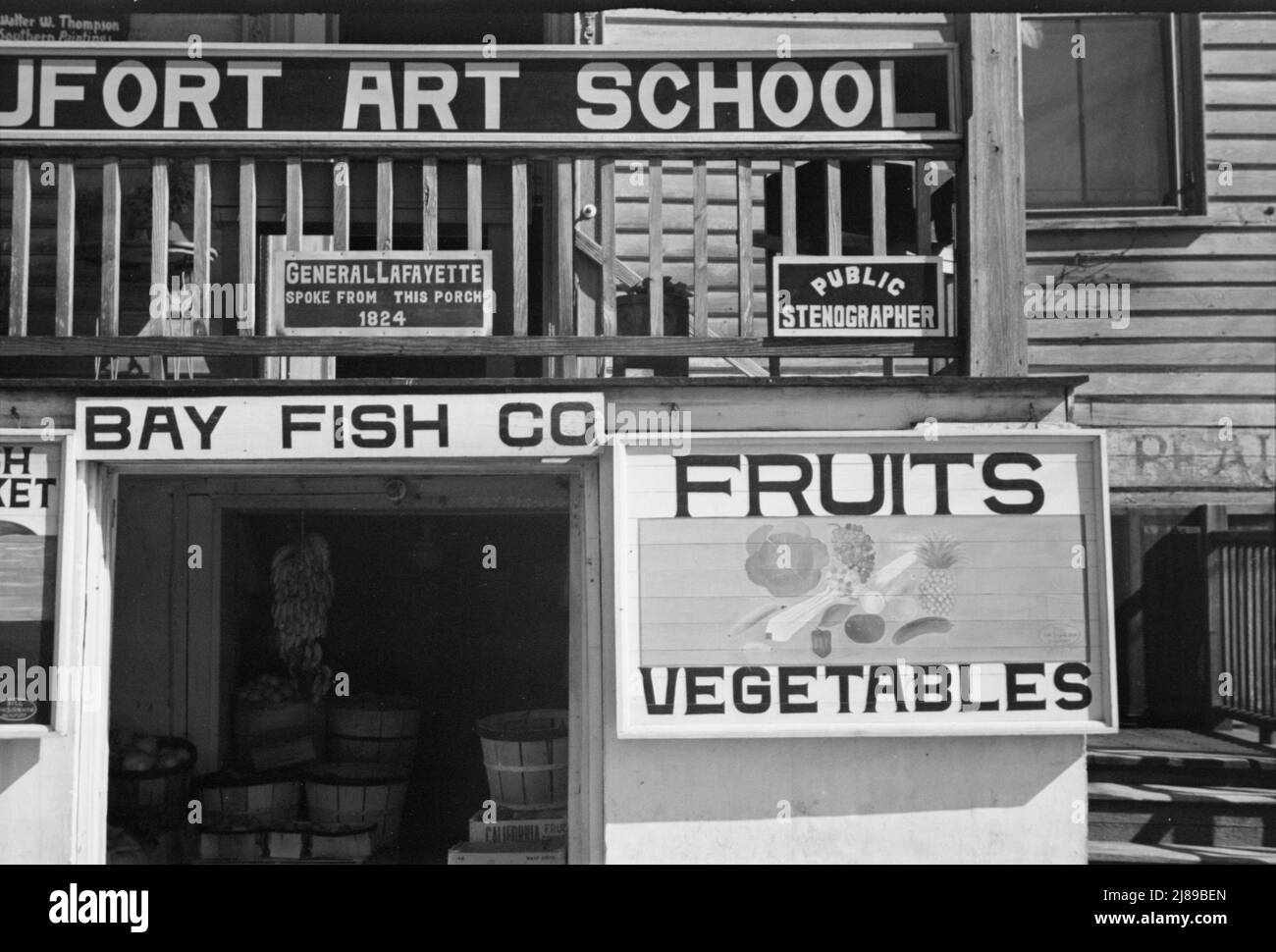 Obstschild. Beaufort, South Carolina. [Schilder: 'Beaufort Art School;. General Lafayette sprach von dieser Veranda 1824; Public stenographer; Bay Fish Co; Obst - Gemüse'. 1824 machte der französische Marquis de Lafayette, der letzte überlebende Generalmajor des amerikanischen Revolutionskrieges, eine Tournee durch die 24 Staaten der Vereinigten Staaten. Er hielt eine Rede vom Balkon des John Mark Verdier House, auch bekannt als Lafayette Building]. Stockfoto