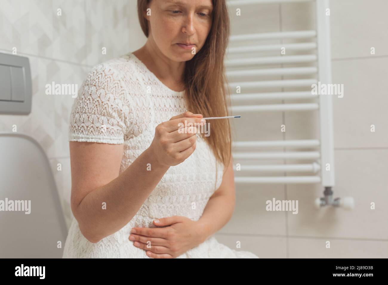 Besorgt Frau mittleren Alters mit Schwangerschaftstest in Toilette Stockfoto