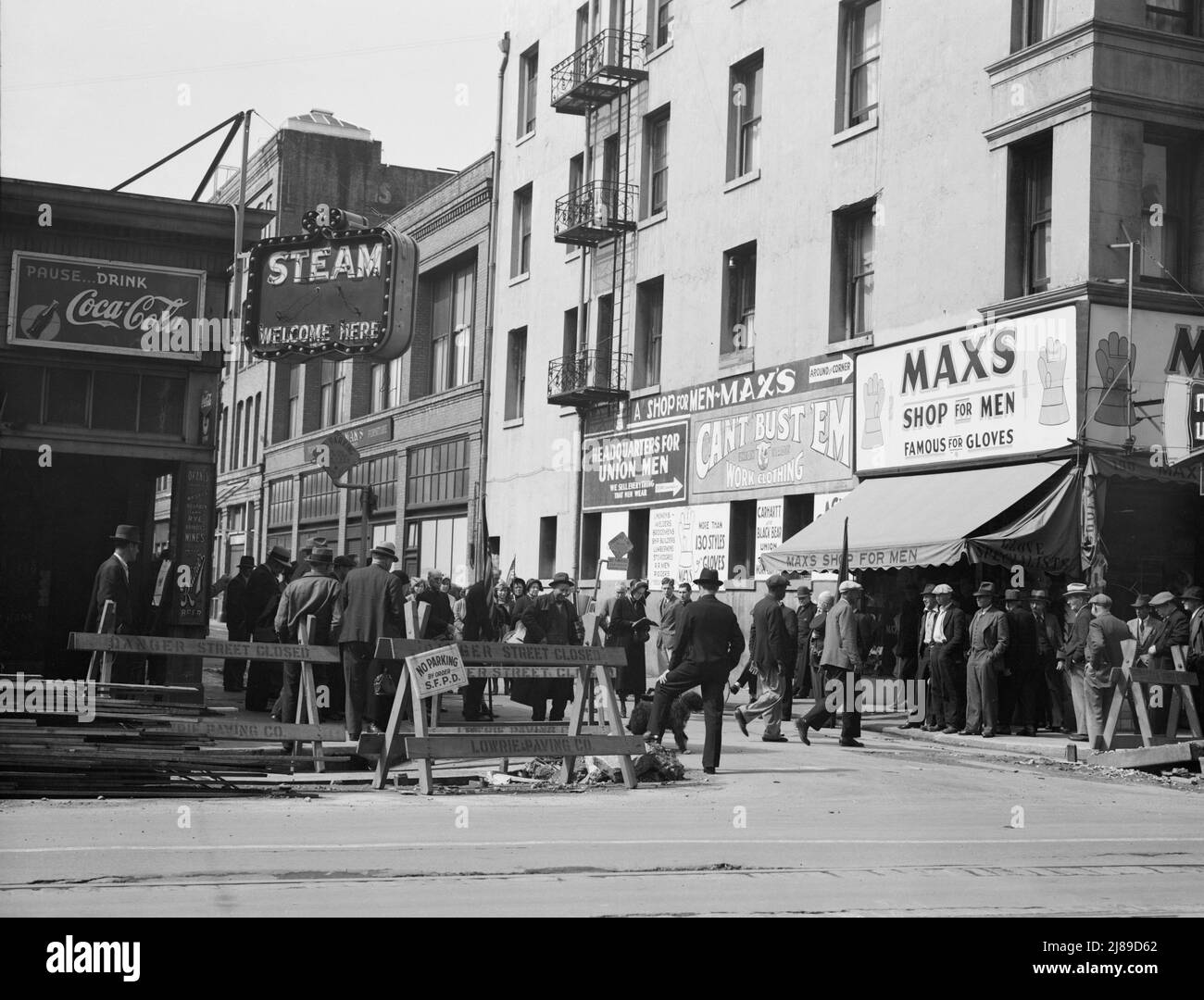 Salvation Army, San Francisco, Kalifornien. Allgemeine Sicht auf Armee und Menschenmengen. [Schilder: 'Danger - Street Closed; Pause...Drink Coca-Cola; Steam Welcome here; Okanes importierte Whiskys - Bourbon und Rye - Brandies - Weine vom Fass - Rainier Beer; Hauptquartier für Union Men - Wir verkaufen alles, was Männer tragen; Can't Bust 'EM Work Clothing; Max's Shop for Men - Famous for Gloves']. Stockfoto